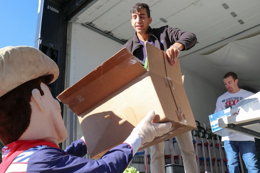 A man hands over a box to another person dressed in a Big Tex costume as part of a donation...