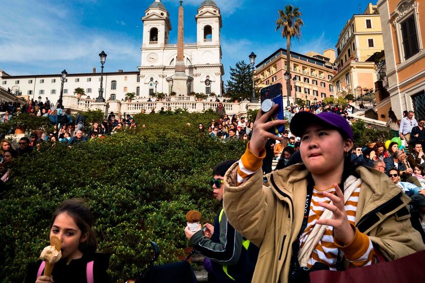 A tourist takes a photo with her smartphone as people sit on the Spanish Steps in Rome. 