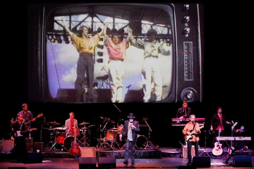 A large screen displays video images of the musical group The Monkees during their...