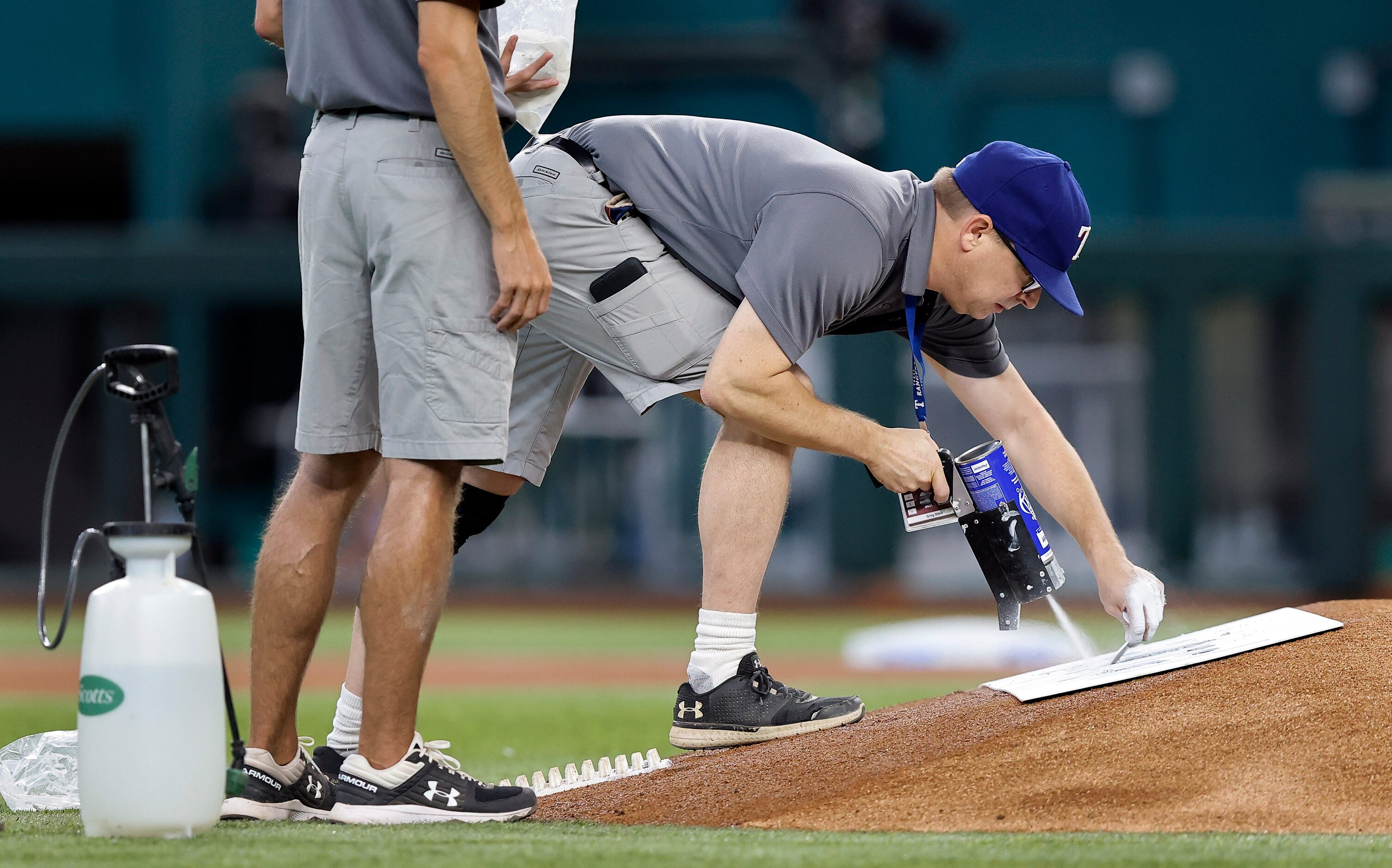 The Texas Rangers grounds crew stencils an advertisement on the back of the pitching mound...