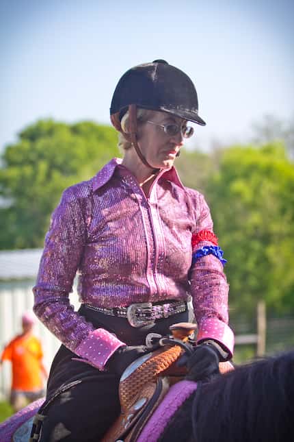 Stacey Johnson, in a pink riding shirt and brown riding helmet, sits atop a dark brown horse.