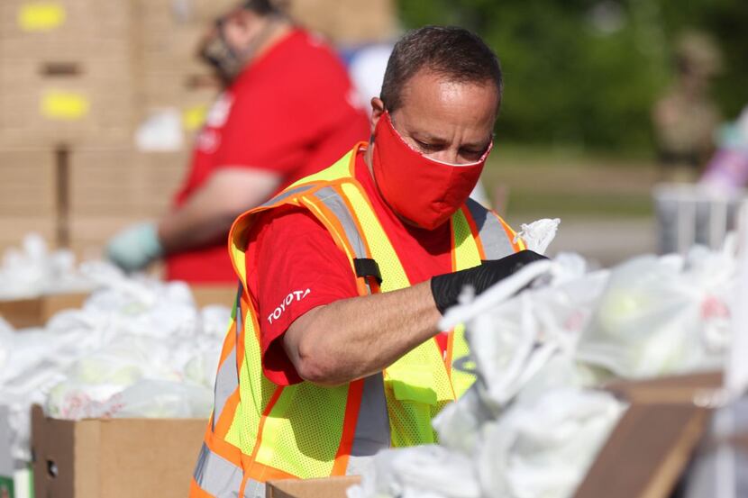 A masked employee at Toyota wears a safety vest while sorting through donation boxes.