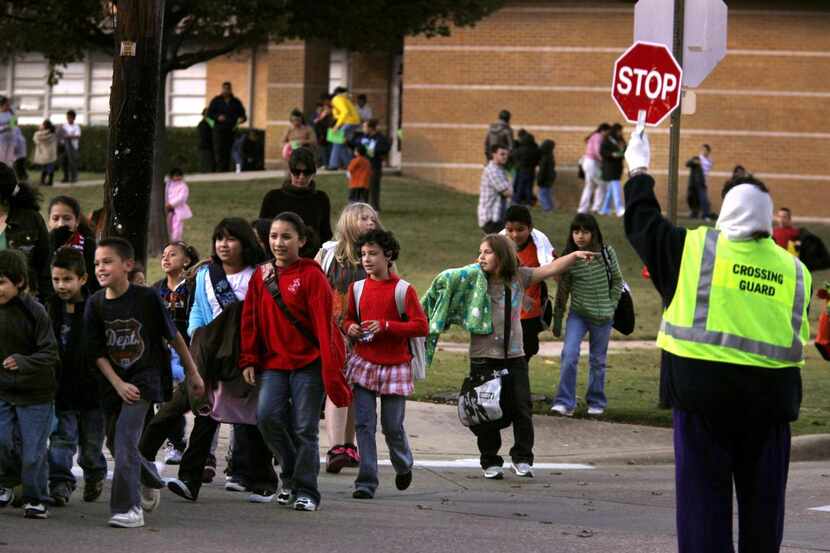 In this file photo, a crossing guard helps students safely cross the street after dismissal...