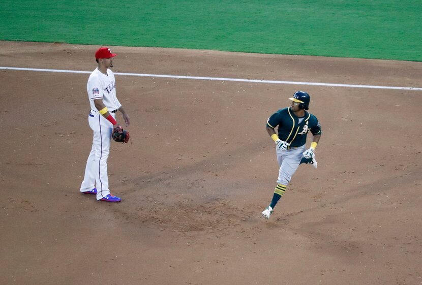 Texas Rangers' Ronald Guzman, left, looks on as Oakland Athletics' Khris Davis rounds the...