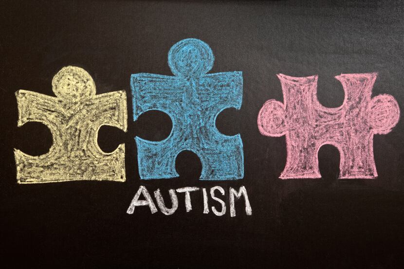  A yellow, blue and red puzzle pieces and the word Autism drawn on a chalkboard.
