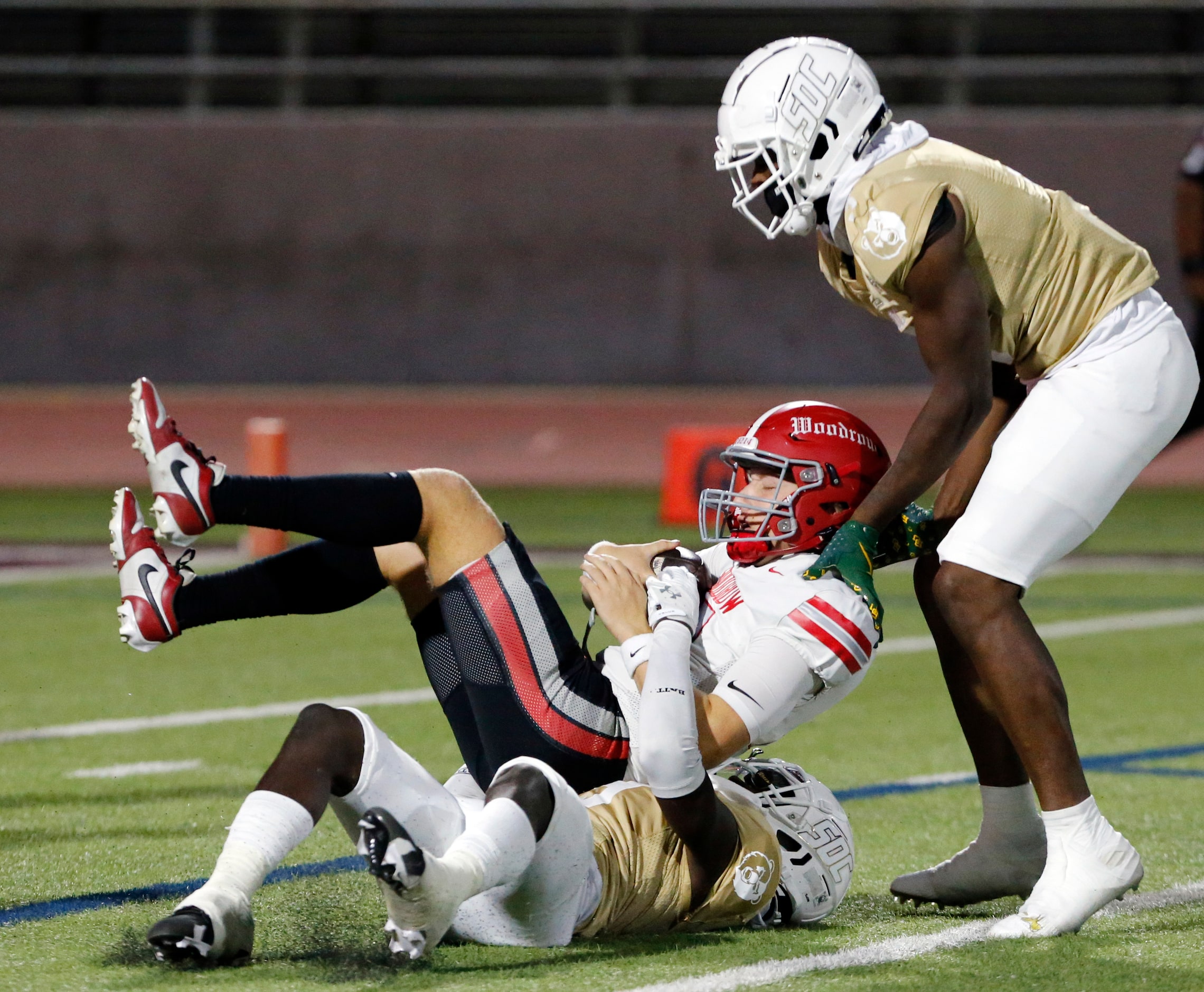 Two South Oak Cliff High defenders tackle Woodrow Wilson High QB Kyle Trulock (12) during...