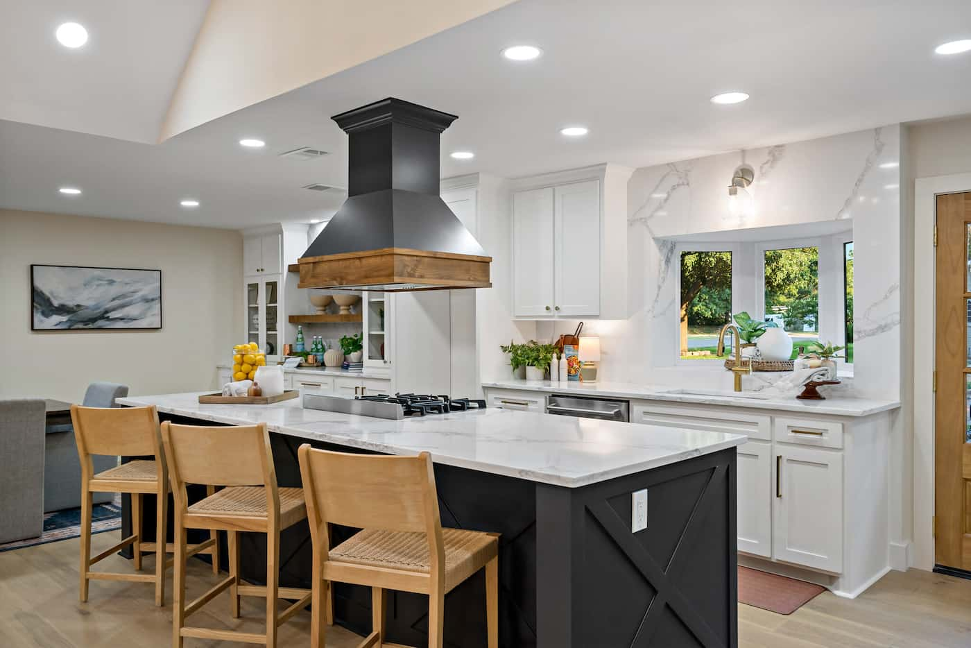 Open kitchen with large island with black lacquered base, white cabinets on the opposite wall...