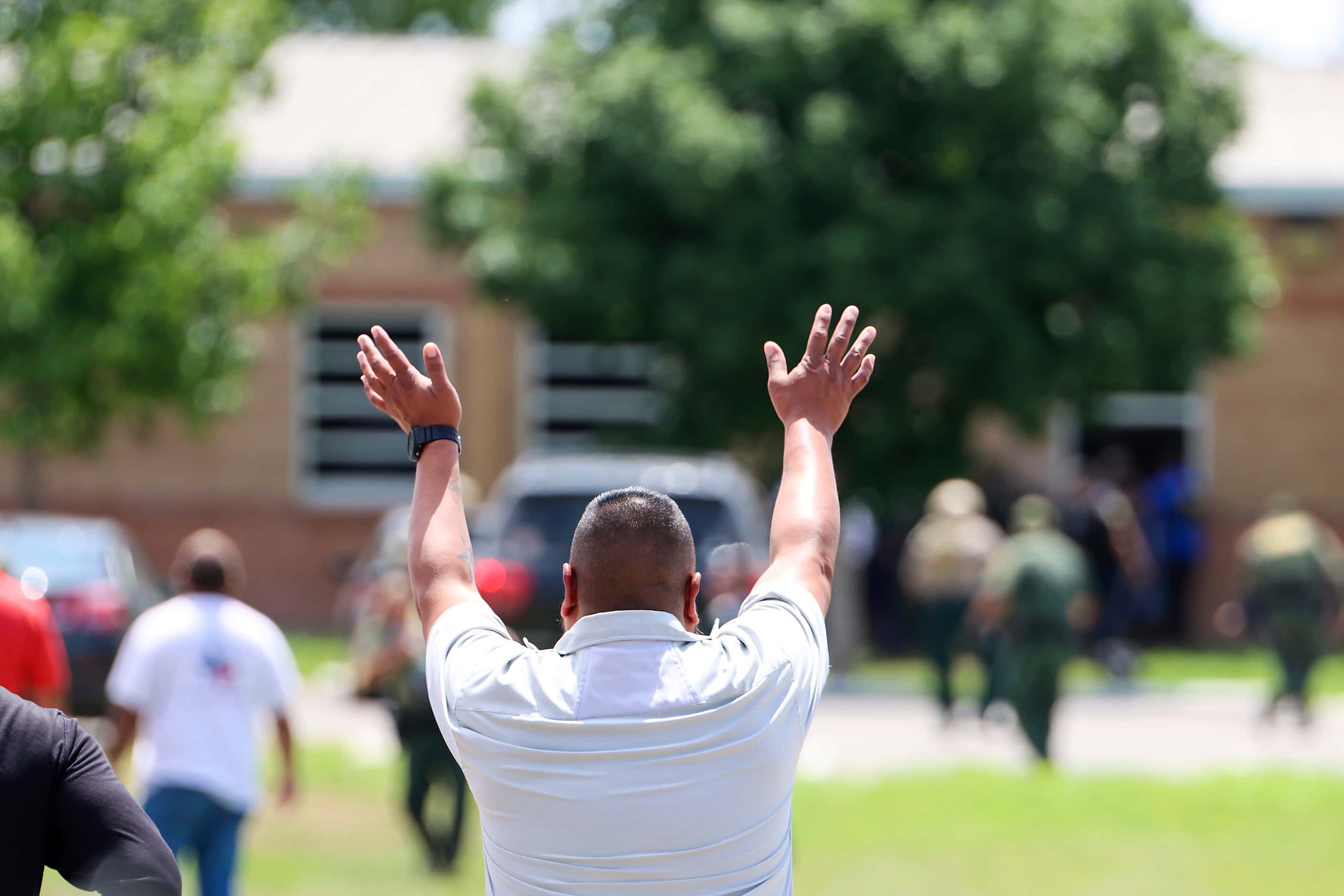 An observer raises his hands as school children are evacuated by law enforcement officers...