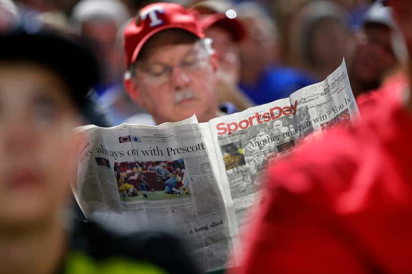 A Texas Rangers fan reads Sportsday section of the newspaper during the fifth inning of the...