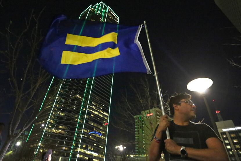 Samuel Sanchez holds a flag with an equality symbol in the evening breeze as protesters...