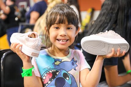 Little girl smiles and holds up a new pair of sneakers she received through donations