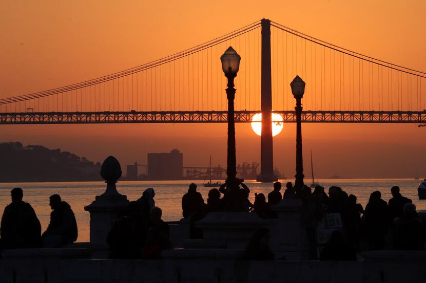 People gather at Lisbon's Comercio square to watch the sun set behind the April 25th Bridge....