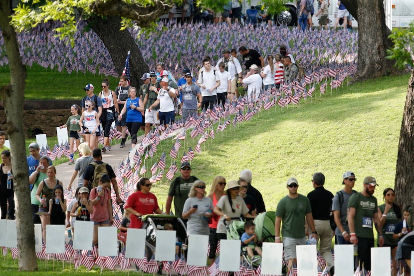 Participants walk past flags and signs planted in the grass honoring police officers and...
