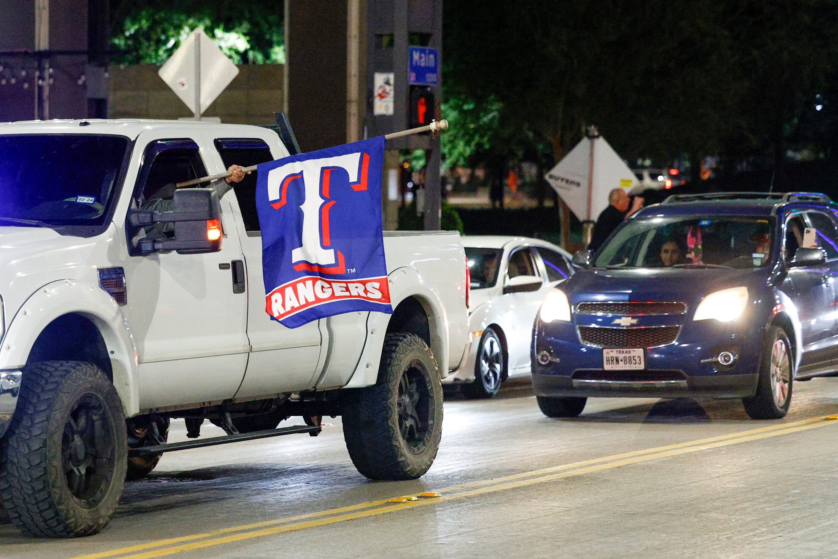 A driver sticks a Texas Rangers flag out of their window as people celebrate on Main Street...