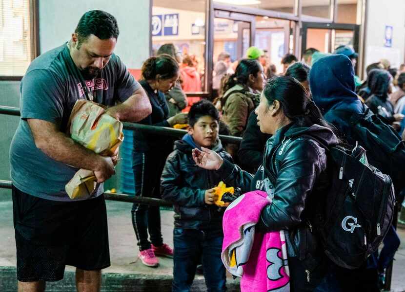 A local man hands out hamburgers to Central American migrants waiting outside the Greyhound...