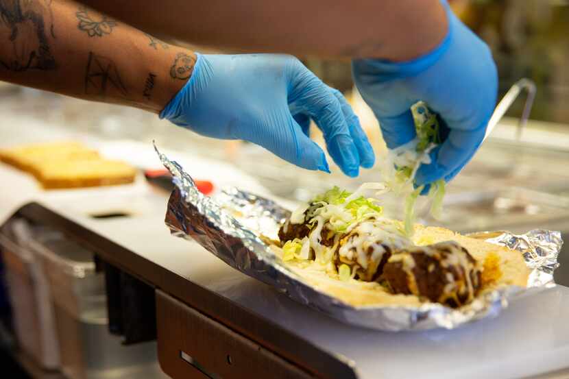 An employee sprinkles lettuce onto a meatball sub at Patriot Sandwich Company in Denton.