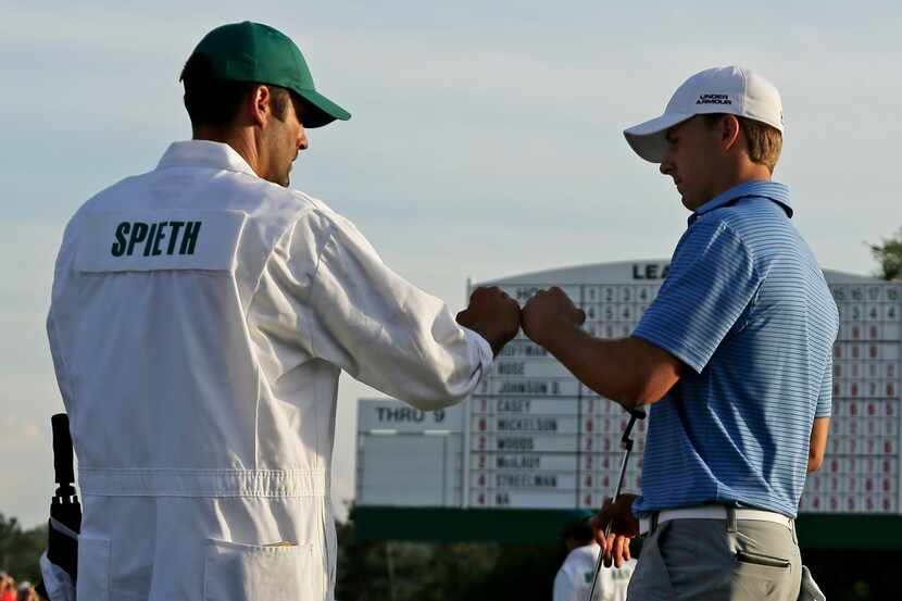 Jordan Spieth touches fists with his caddie Michael Greller after putting out on the 18th...