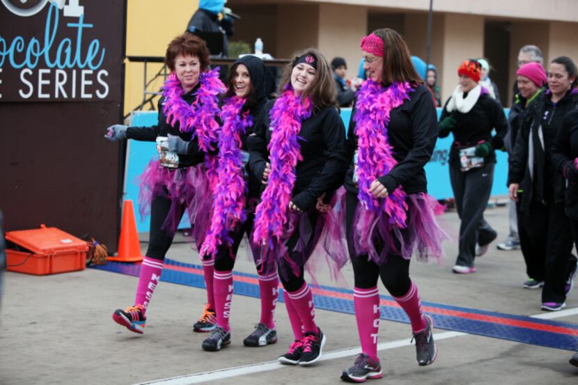 A group of women wearing matching feather boas and tutus cross the finish line to complete...