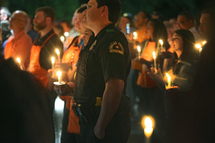 A Dallas policeman stands among Home Depot employees during a candlelight vigil to support...