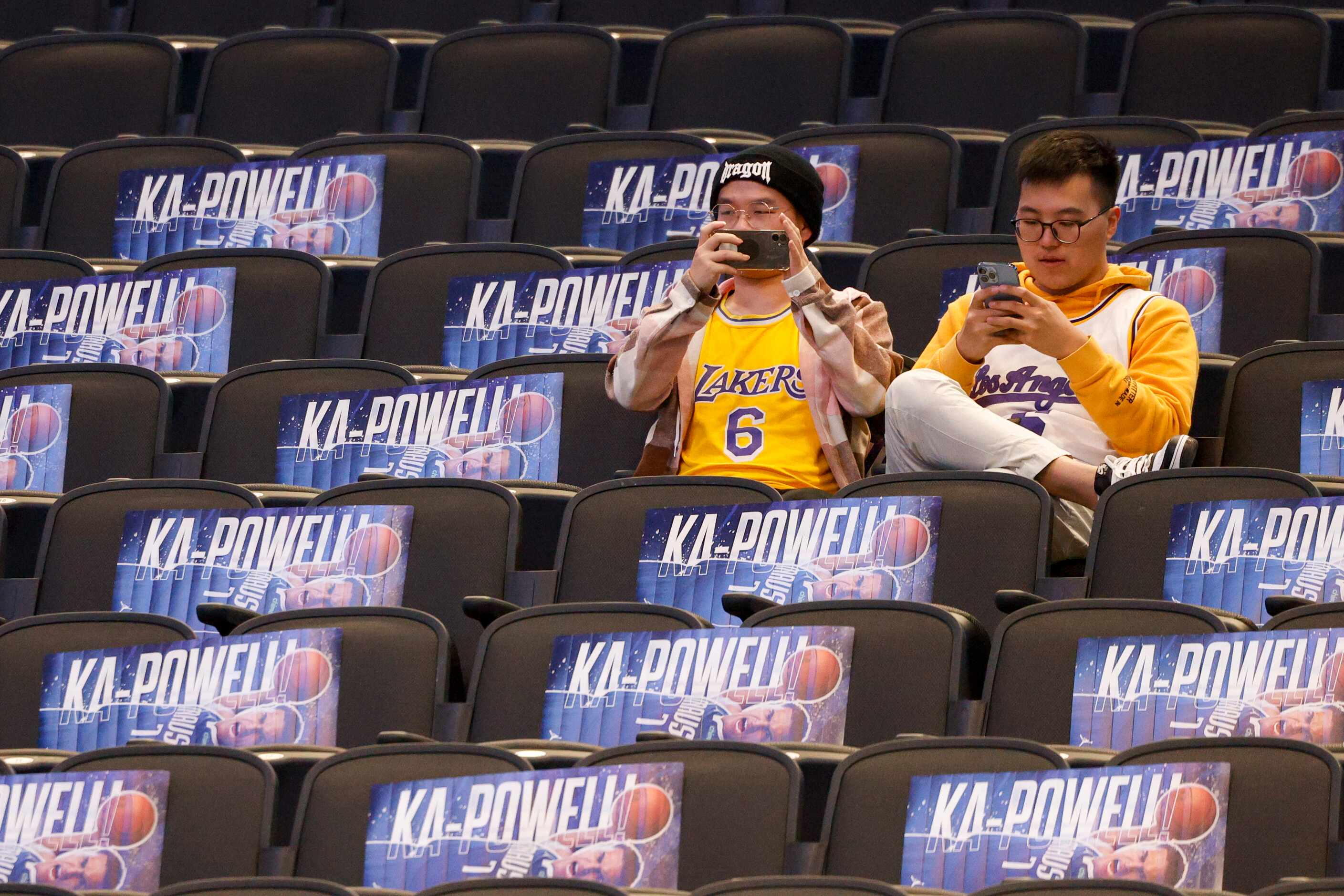 A pair of Los Angeles Lakers fans sit among posters of Dallas Mavericks center Dwight Powell...