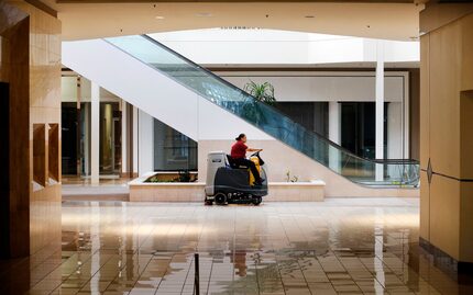 Passing by empty stores, housekeeper Juana Lemoine polishes the floor of an empty Collin...