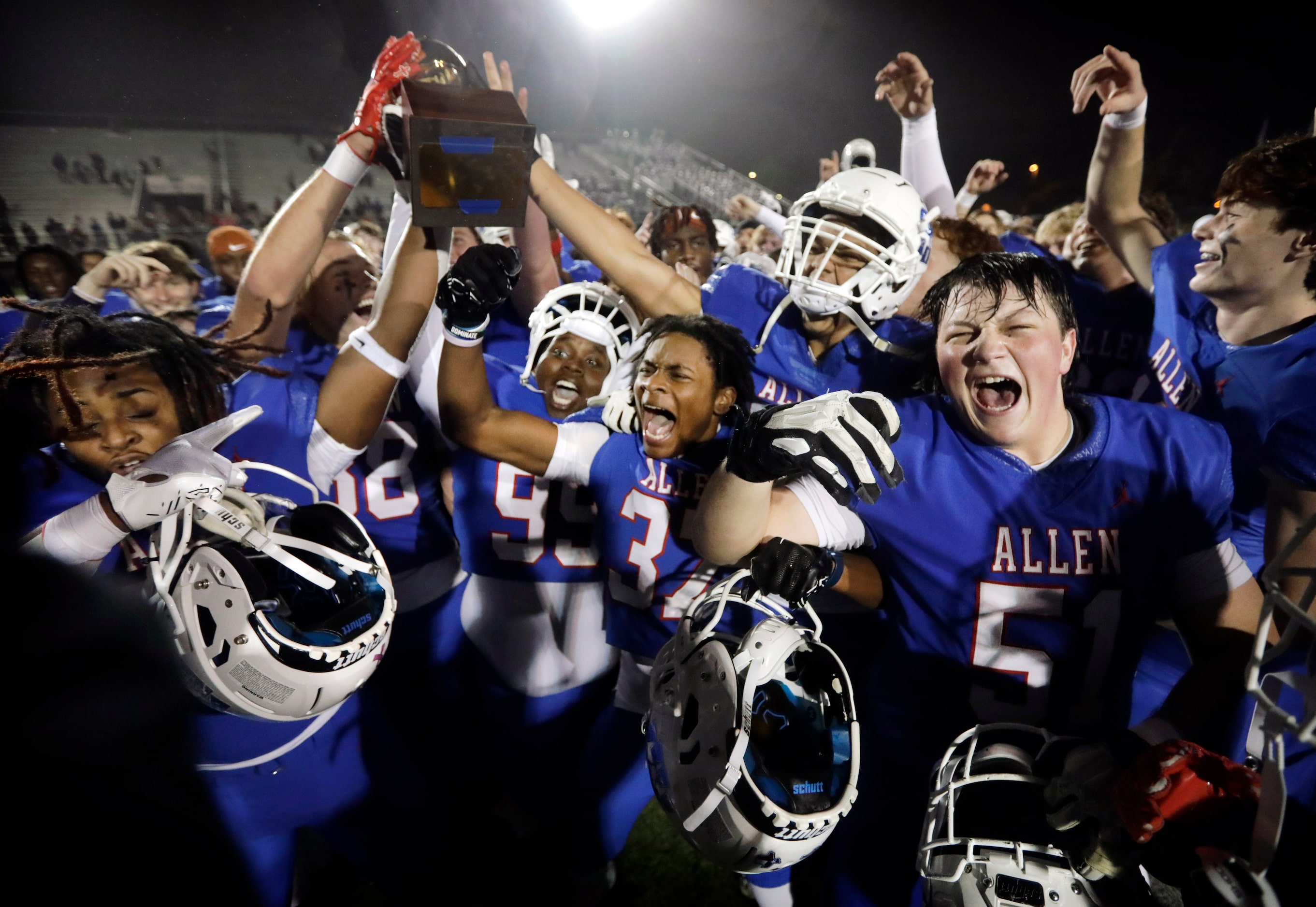 Allen football players celebrate with the winning trophy after defeating Arlington Martin in...