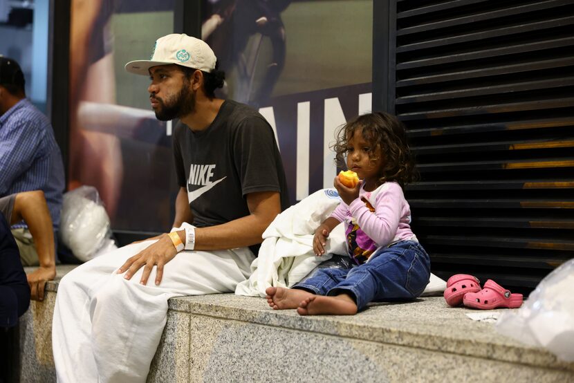 Cataleya takes a bite of a necatrine alongside her father Elier as they wait for a bus to...