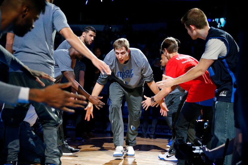 Dallas Mavericks forward Dirk Nowitzki slaps hands with fans and teammates as he is...