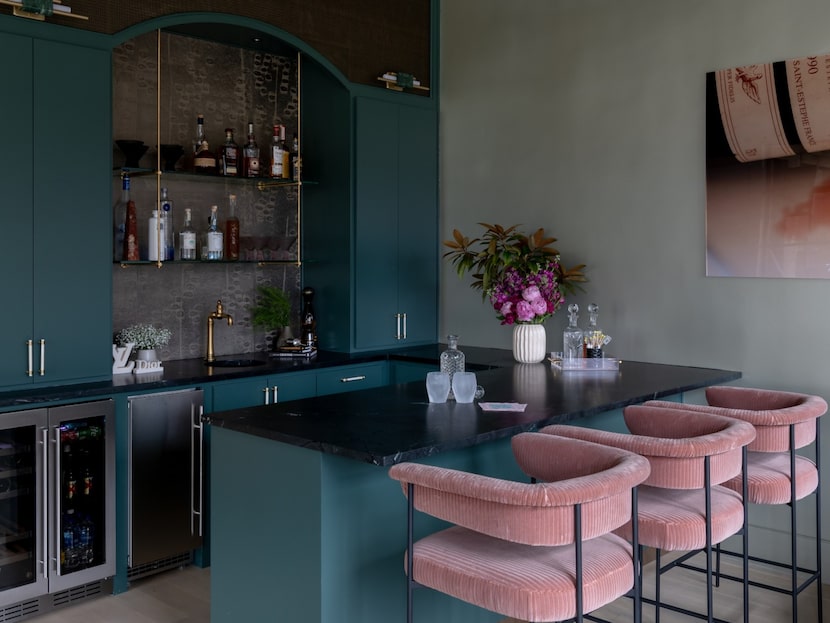 Home bar with deep teal cabinetry. pink velvet bar chairs and pink artwork