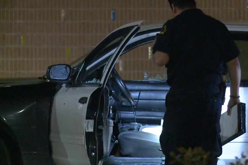 An officer shines a flashlight into a car at the scene of a shooting call at the...