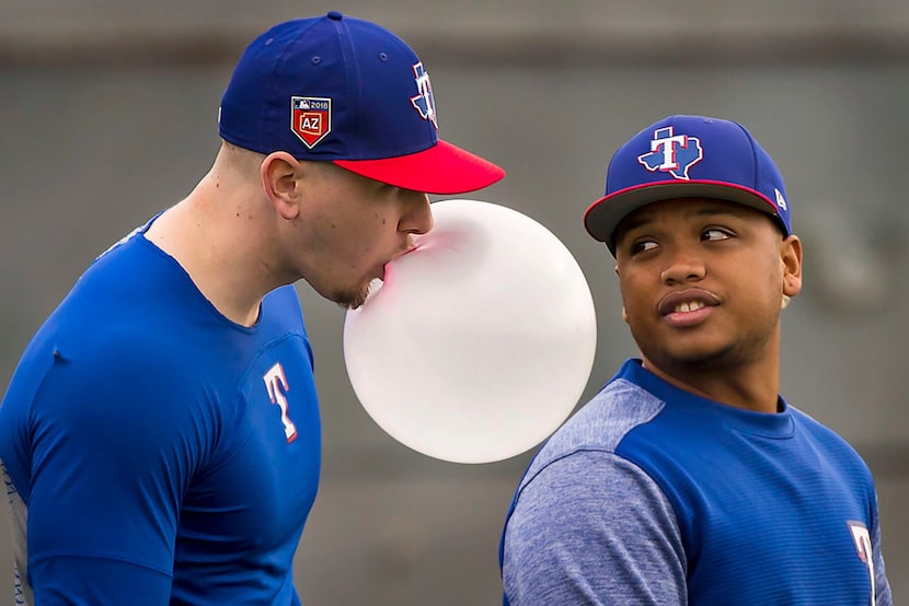 Texas Rangers outfielder Ryan Rua blows a bubble as outfielder Willie Calhoun looks on...