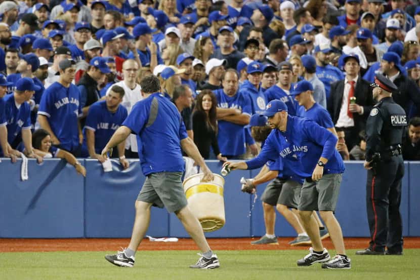 The Toronto grounds crew picks up beverages thrown onto the field after the umpires...
