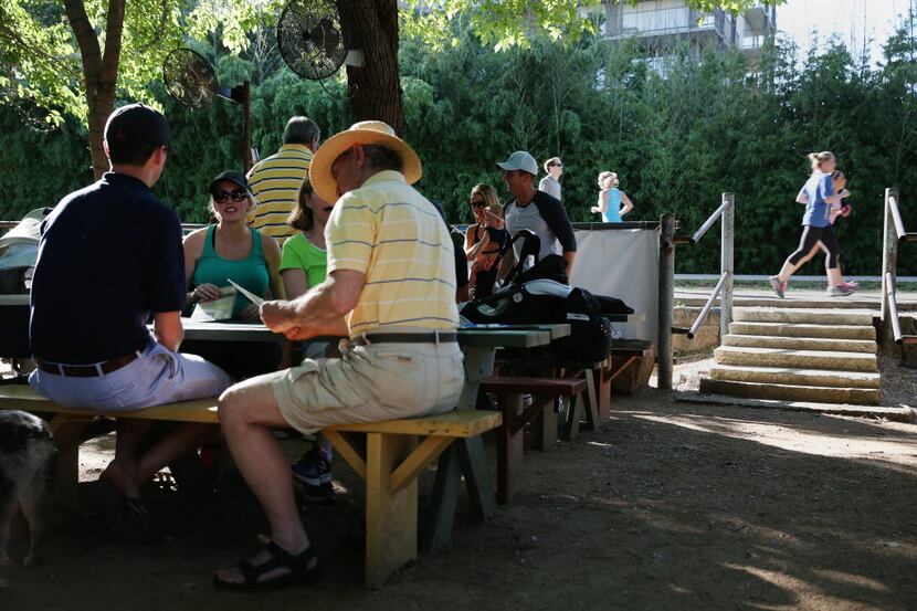 Guests at the Katy Trail Ice House sit at a table as pedestrians and joggers use the Katy...