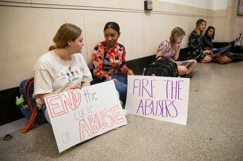 UT Austin juniors Ky Higdon (left) and Courtney LeBlanc hold signs outside of Executive Vice...