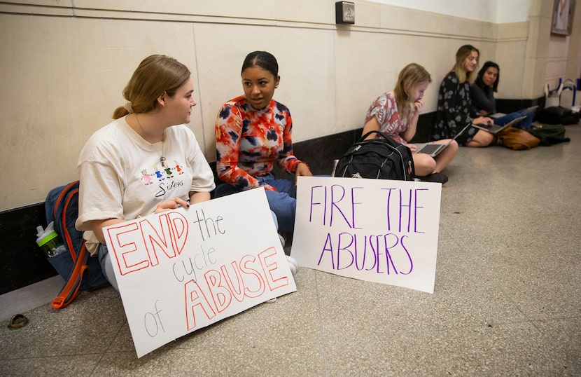 UT Austin juniors Ky Higdon (left) and Courtney LeBlanc hold signs outside of Executive Vice...