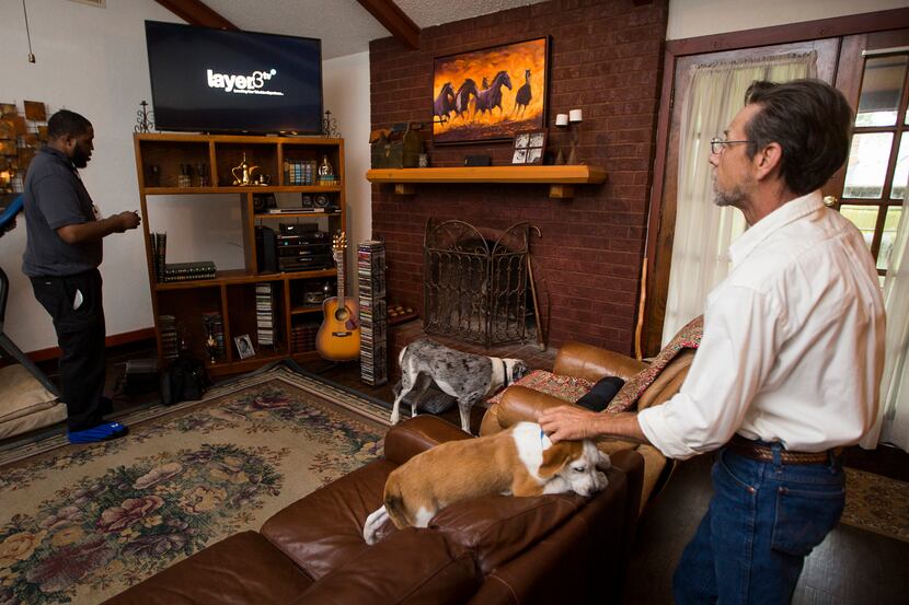 Stevan Grimes scratches his dog Norman as Keith Hamilton of Layer3 installs cable TV...