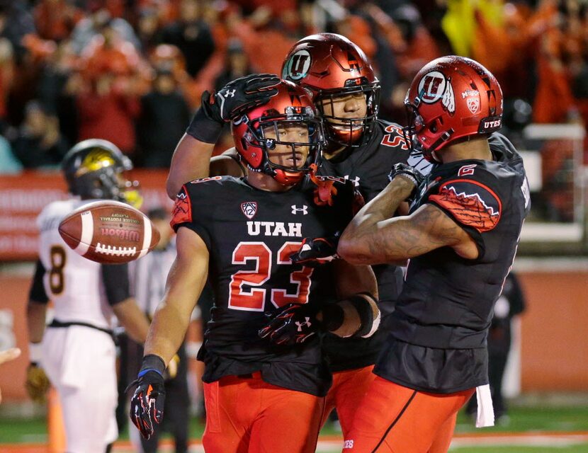 Utah running back Devontae Booker (23) receives a hug from teammates Sam Tevi (52) and...