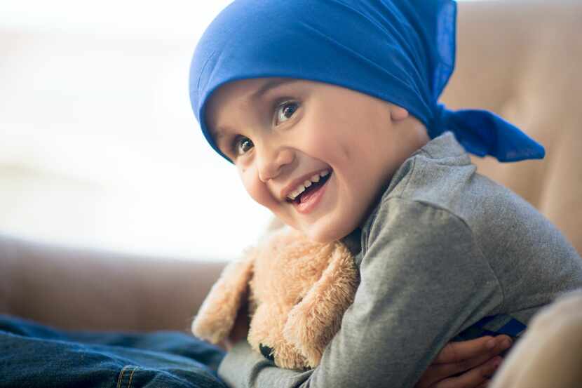 A little boy with a blue scarf on his head hugs his teddy bear after a chemotherapy treatment.