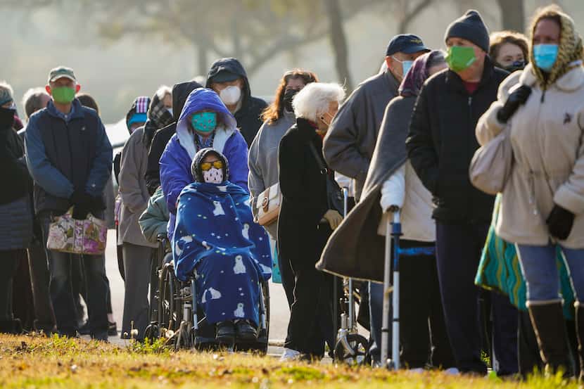People bundle up against a cold morning as they wait in a long line to receive the COVID-19...