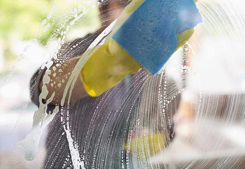 Person in yellow gloves uses a blue sponge, soap and water to clean an exterior window