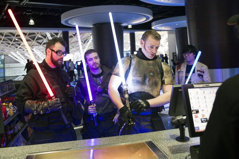 Customers holding lightsabers and dressed as Jedi Knights, collect their tickets from the...