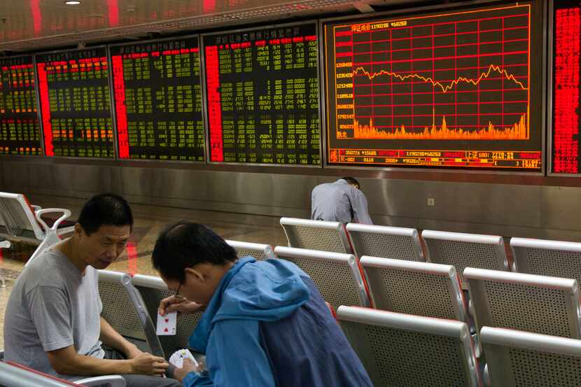 Investors play a card game near electronic boards displaying stock prices in Beijing,...
