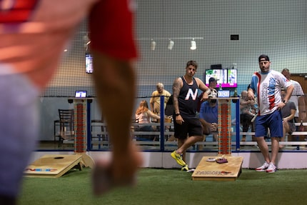 Cody Hughes and Trey Sparks watch as Mac tosses a bag during a cornhole tournament hosted by...