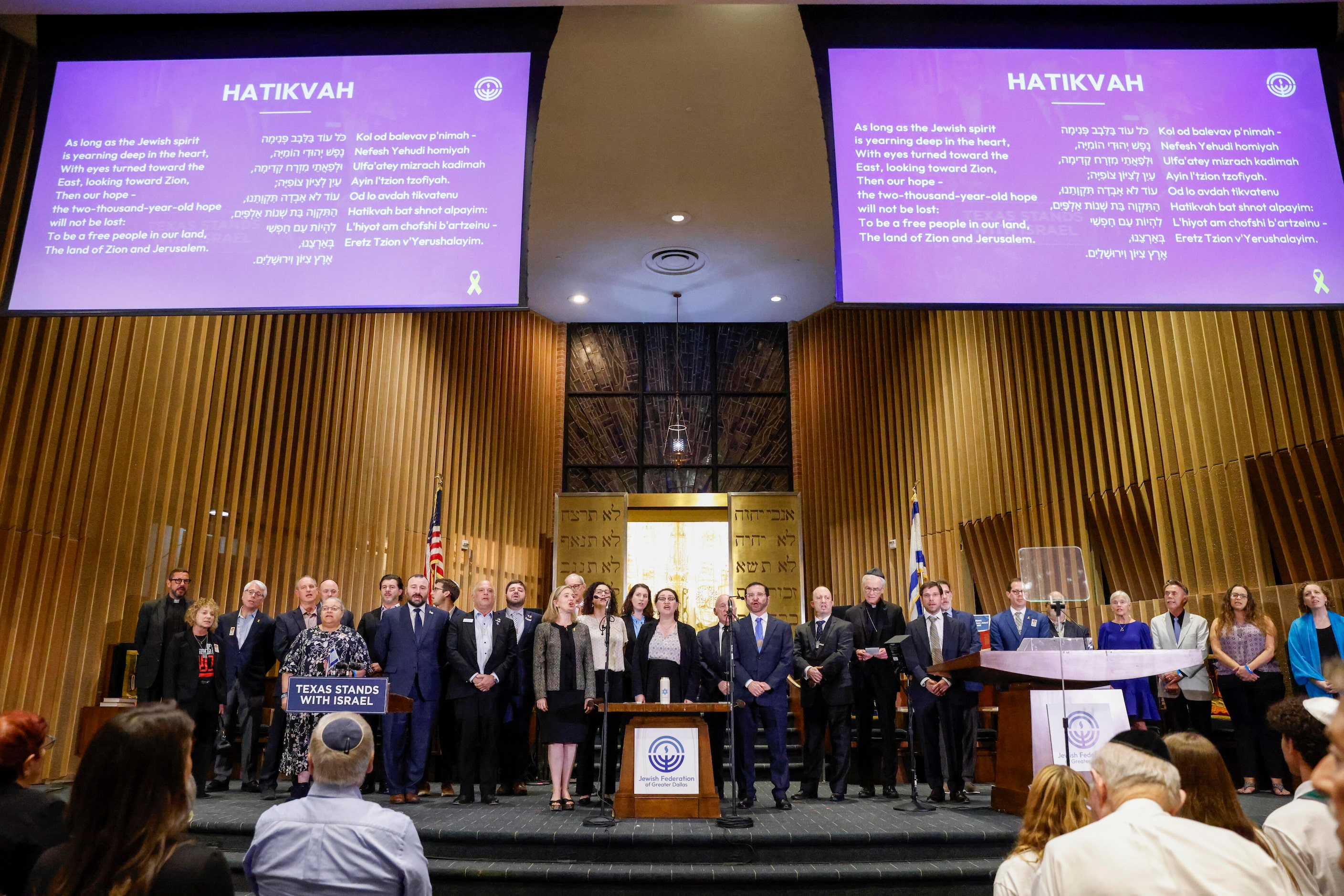 People stand and sing the Israeli national anthem during a community event commemorating the...