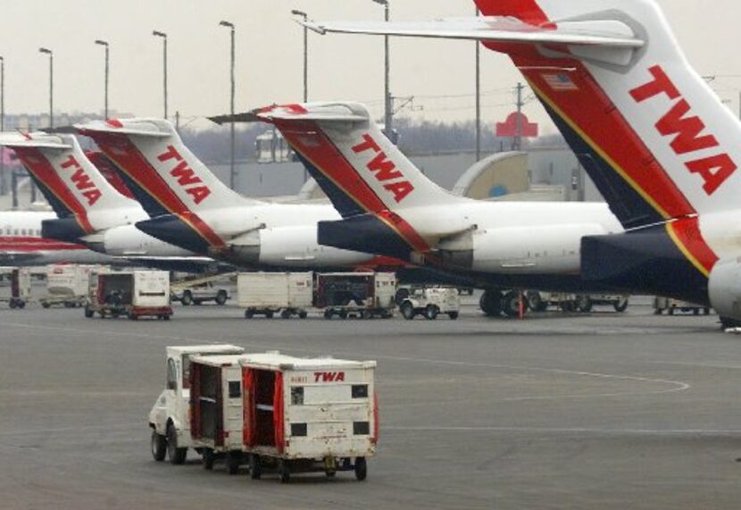  A Trans World Airline baggage cart crosses the tarmac behind a line of TWA jets Monday,...