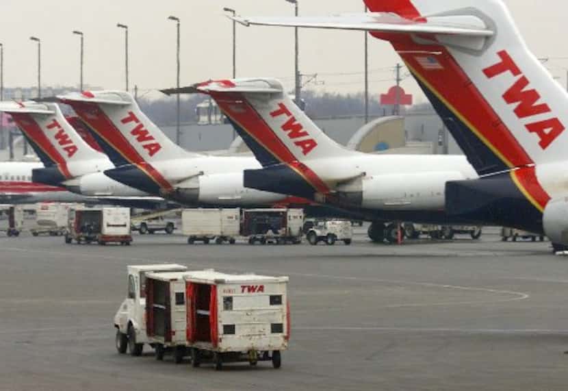  A Trans World Airline baggage cart crosses the tarmac behind a line of TWA jets Monday,...