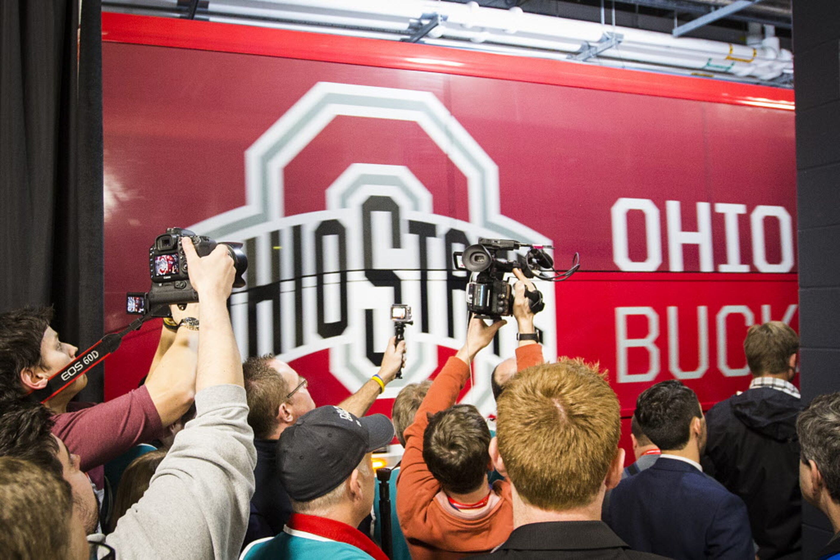 Photographers train their cameras on the Ohio State Buckeyes buses as they roll past the...