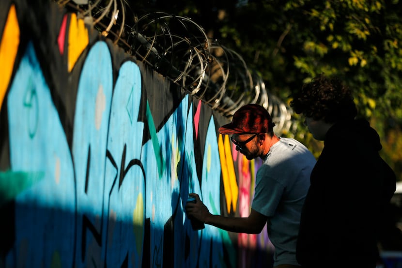 An artist creates spray art on a wooden fence Saturday at The Fabrication Yard in West...