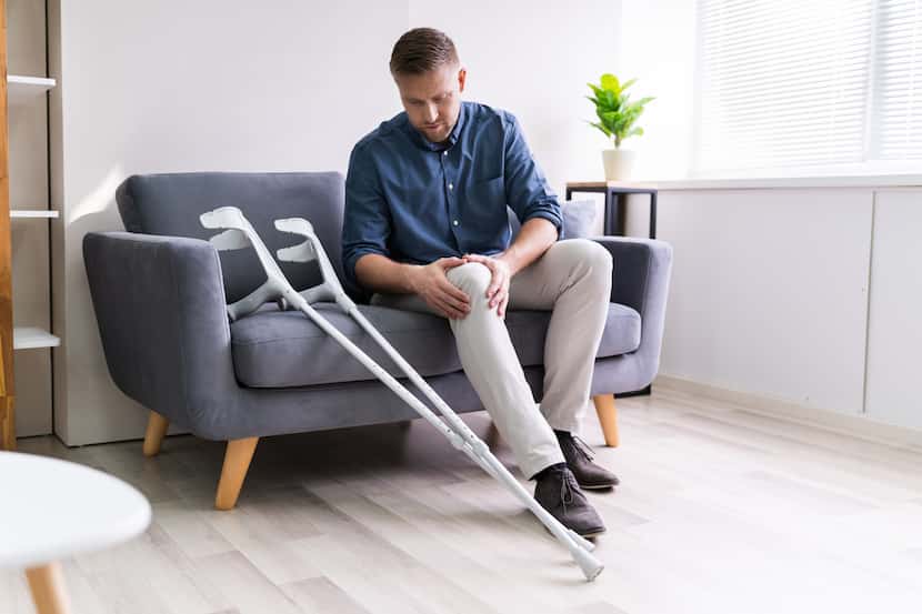 Man suffering from knee pain sitting on sofa with crutches.