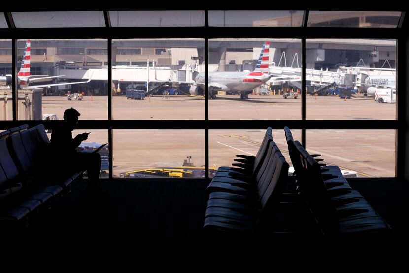 A single traveler sits next to empty chairs at an American Airlines gate in terminal C at...